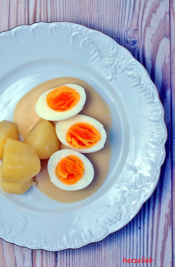 Auf diesem Bild zu Omas Senfeier Rezept sieht man einen Teller, der von oben fotografiert ist. Angerichtet sind 3 halbe Eier mit Senfsoße und Kartoffeln.