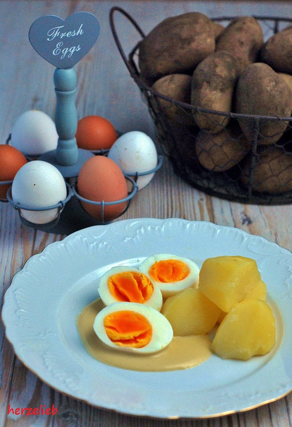 3 halbe Eier in Senfsauce mit Kartoffeln sieht man au diesem Foto zum Senfeier Rezept. Im Hintergrund ein Korb Kartoffeln und Eier in einer Etager