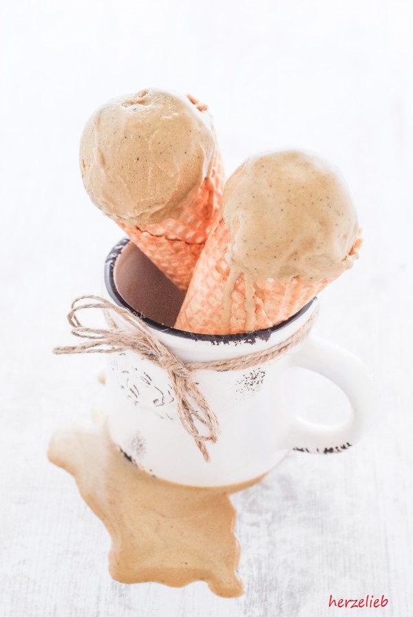 Auf diesem Bild zum Muckefuck Eis Rezept sieht man zwei Eistüten mit dem beigefarbenen Eiskugeln, die in einer Tasse stehen. An an der Tasse ist da Eis heruntergelaufen