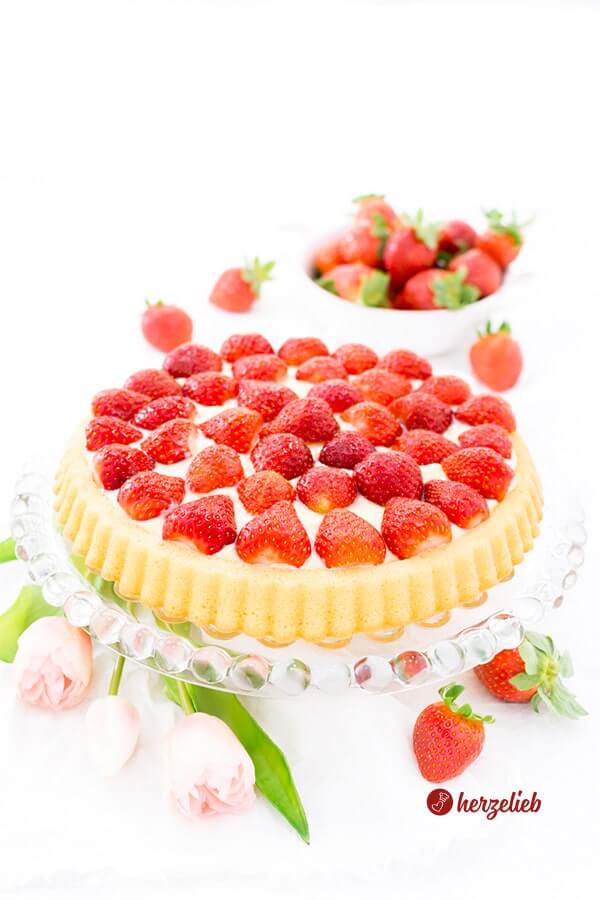 Erdbeerkuchen nach einem Obstboden Rezept mit Pudding und Erdbeerenvon herzelieb. Dekoriert mit Blumen. Im Hintergrund eine Schale mit frischen Beeren.