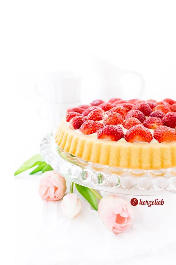 Erdbeertorte mit einen Obstboden Rezept mit Pudding von herzelieb. Der Erdbeerkuchen steht auf einem Glasboden. und ist dekoriert mit Blumen.