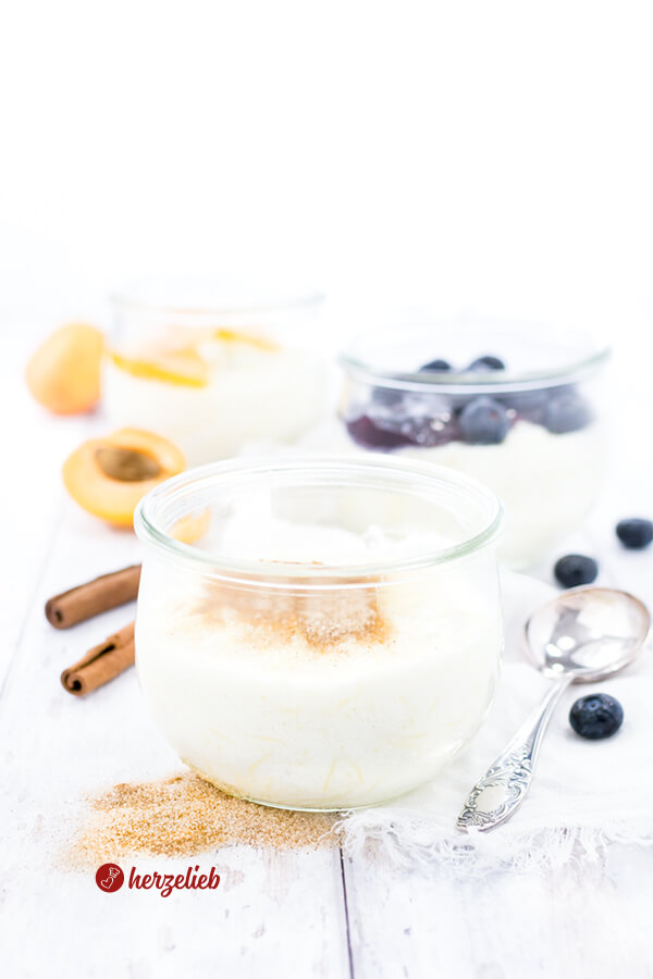 3 Portionen Nudelpudding im Glas mit Zimt und Zucker, eines mit Blaubeeren und eines Aprikosen. Dekoriert mit Zimtzucker, Aprikosen, Zimtstangen und Blaubeeren. 