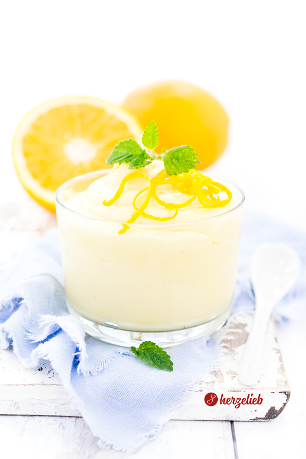 Schnelles Orangen Dessert im Glas Rezept von herzelieb. Angerichtet auf einem weißen Brett mit einem hellblauen Tuch, mit Orangenzesten und Zitronenmelisse. Im Hintergrund eine ganze und eine halbe Orange.
