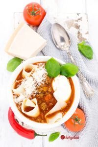 Lasagnesuppe in einer Schale mit Parmesan, Tomate, Chilie und Basilikum und Creme Fraiche