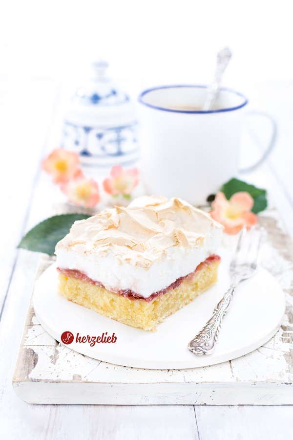Auf dem Bild zum Bedstefars Rezept aus Dänemark ist ein Stück des Blechkuchens auf einem weißen Teller mit einer Kuchengabel zu sehen. Im Hintergrund Blüten, ein Becher Kaffee und ein Zuckertopf. Der Kuchen hießt übersetzt "Opas Bart"