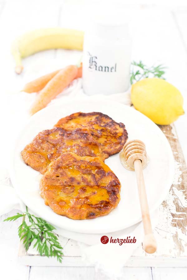 Saftige Karottenkuchen Pfannkuchen auf einem Teller mit einem Honiglöffel, Karotten, zitronen, Banananen vom Foodblog herzelieb
