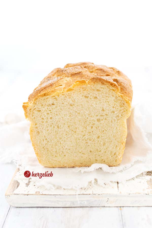 Dieses Foto zum Pfeffer-Salz-Brot Rezept ist von vorne fotografiert. Das Brot ist angeschnitten und hat eine goldbraune Kruste und eine lockere Krume. Es liegt auf einem weißen Tuch, das auf einem weißen Holzbrett liegt.