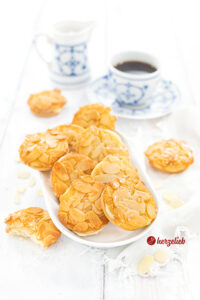 Bienenstich-Plätzchen in einer weißen Schale. Im Hintergrund ein Milchkännchen und eine Tasse Kaffee.