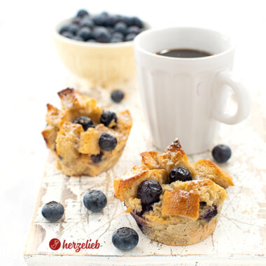 Dieses Foto zum Arme Ritter Muffins Rezept zeigt 2 Muffins mit einer Tasse Kaffee und einer gelben Schale mit Blaubeeren