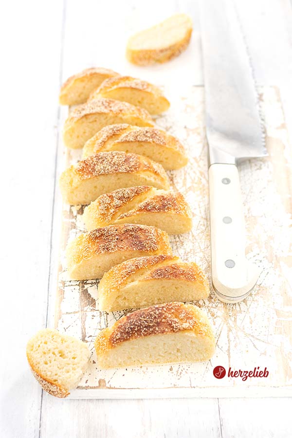 Auf diesem Foto zum Baguette-Stangen Rezept sieht man ein aufgeschnittenes Baguette, die Scheiben stehen versetzt hintereinander. Rechts von den Brotscheiben liegt ein Brotmesser. 