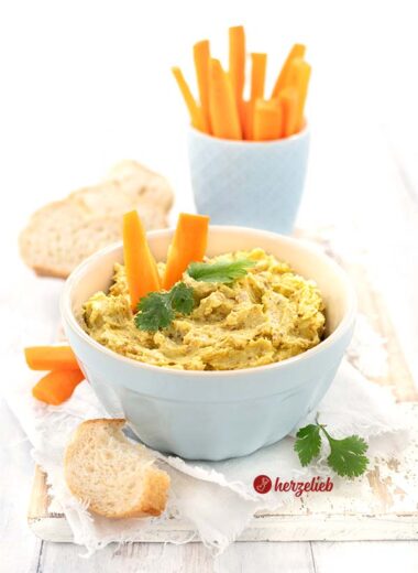 Ein leckerer Currydip mit Fetakäse in einer blauen Schale ist auf diesem Bild zum Feige-Curry-Dip Rezept zu sehen. Dekoriert mit Brot, Karottensticks und frischem Koriander