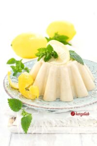 Auf diesem Bild zum Zitronenpudding Rezept ist der selbstgekochte Pudding wie von Oma zu sehen. Er ist auf einem türkisfarbenen Teller angerichtet und Dekoriert mit Zitronenschale und Zitronenmelisse