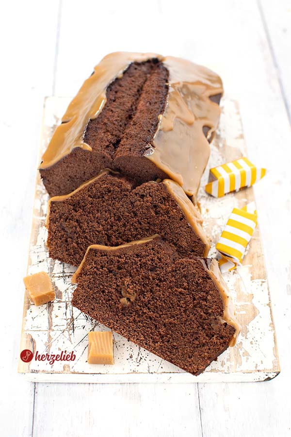 Dieses Foto zum Muh-Kuchen Rezept ist von schräg oben fotografiert. Vor dem angeschnittenen Kuchen liegen schräg zwei Scheiben. Der Schokoladenkuchen ist mit einem Karamellguss überzogen. 