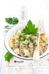 Eine weiße Schale mit einem blauen Rand, in der ein Gemüseeintopf mit Hacfkleisch zus ehen ist, sieht man auf diesem Bild zum Kohlrabitopf Rezept. Der Eintopf ist mit Petersilie und Pfeffer aus der Mühle bestreut und einem Petersilienblatt dekoriert. Auf dem Schüsselrand liegt eine Silbergabel. Im Hinterrund steht ein Pfefferstreuer, eine Schale mit gehackter Petersilie.