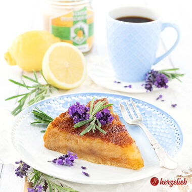 Ein Stück Honigkuchen nach einem Imkerkuchen rezept von herzelieb. Dekoriert mit Lavenblüten und Lavendelblättern. Im Hintergrund eine halben und eine ganze Zitrone, ein Glas Honig und eine Tasse Kaffee