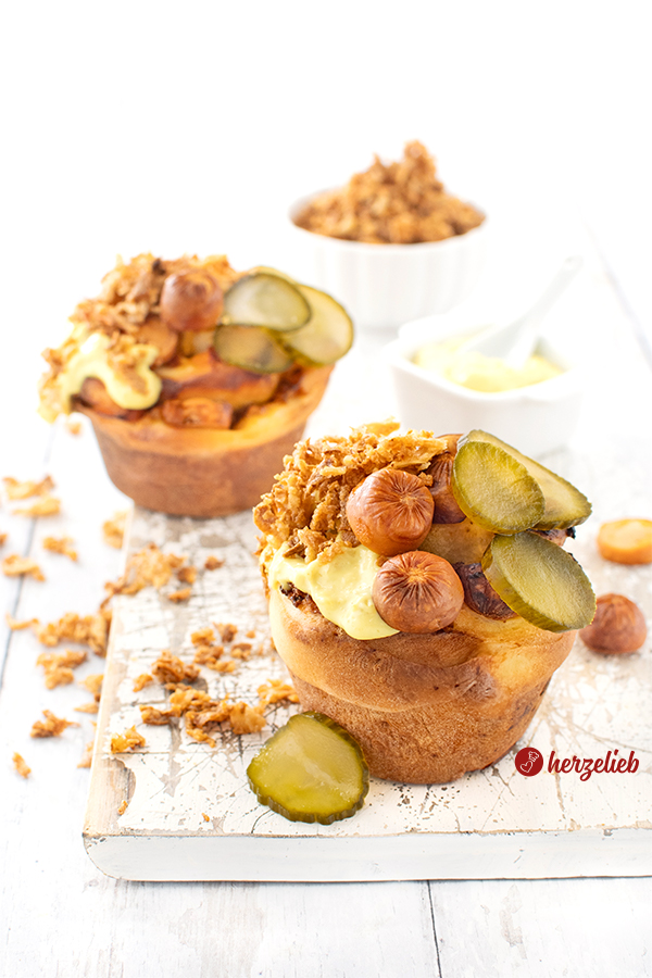 Zwei Hot Dog Muffins auf einem weißen Holzbrett. Das Fingerfood ist garniert mit Röstzwiebeln, dänischen Gurken und dänischer Remoulade. 