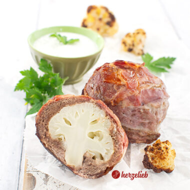 Zwei Blumenkohlbomben nach einem rezept von herzelieb. Das vordere Stück ist halbiert und man sieht im Inneren den Blumenkohl. Vorher rechts ein Stück gebratener Blumenkohl. Im Hintergrund ein grünes Schälchen mit Kräuterdip, davor liegt en Büschel Petersilie. Ganz hinten weitere geröstete Blumenkohlröschen