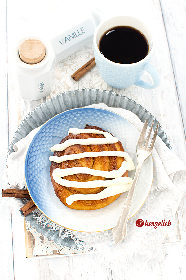 Ein Stück Kuchen mit einem Frischkäse Topping nach einem Nussschnecken Rezept von Herzelieb – angerichtet auf einem Teller mit blauweißem Farbverlauf. Auf dem Tellerrand liegt eine Kuchengabel