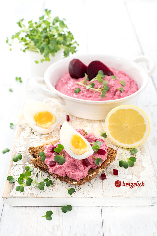 Rote Bete Meerrettich Aufstrich auf Schwarzbrot. Dekoriert mit Kresse, kleinen Rotete Bete Würfeln und Ei. Im Hintergrund eine halbe Zitrone, ein halbes Ei . Ganz hinten eine Schale mit dem Dip bzw. dem Brotaufstrich und ein Büschel Brunnenkresse