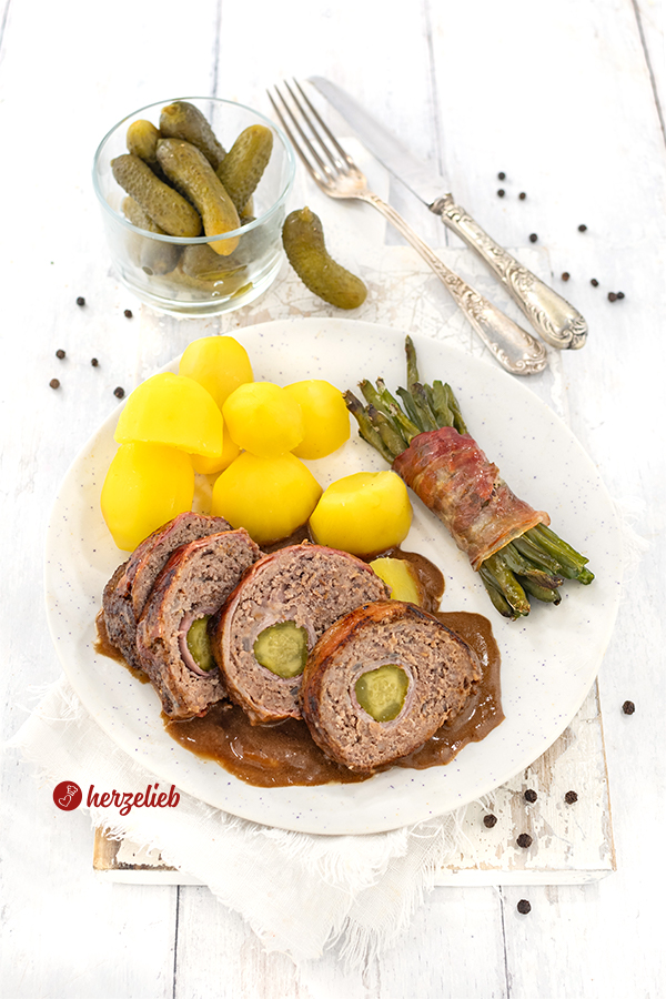 Eine aufgeschnittene Bauernroulade oder Hackroulade nach einem Hackfleischrouladen Rezept von herzelieb. Angerichtet auf einem Teller mit Speckbohnen, Kartoffeln und dunkler Soße