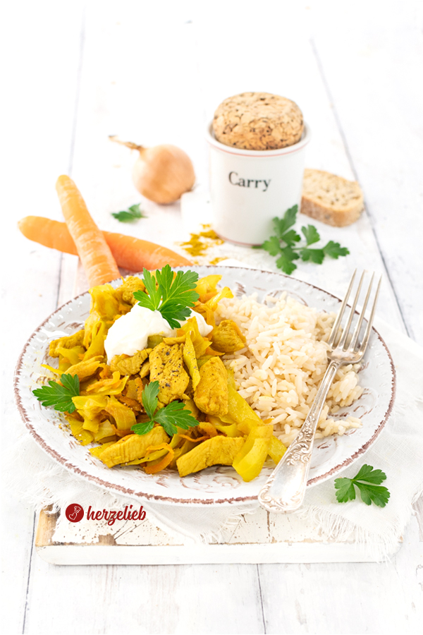 Auf einem Teller ist ein Kohlgericht mit Reis, zubereitet nach einem Karrykål Rezept aus Dänemark von herzelieb, angerichtet. Das Gericht enthält Hühnerstücke, durch Curry gelbfärbten Kohl und Karottenstücke. Oben drauf sind Sauerrahm und frische Kräuter. Serviert wird es mit Reis. Im Hintergrund steht ein Gewürzbehälter für Curry und auf dem Tellerrand liegt eine Gabel.