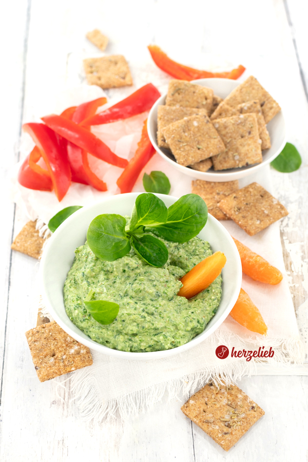 Schneller Frischkäsedip mit Feldsalat nach einem Feldsalat-Dip Rezept von herzelieb. Dekoriert mit einem Büschel Salat. Hinter der Dipschale liegen Gemüsesticks. Rechts hinten steht eine Schale mit Brotcrackern.