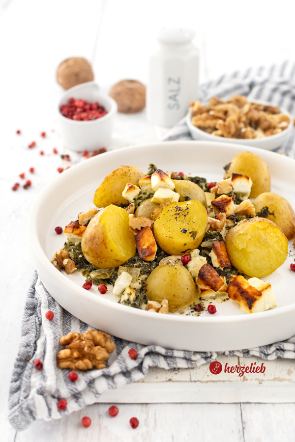 Ein Teller mit Grünkohl-Kartoffelauflauf nach einem Grünkohl Rezept mit Kartoffeln, Fetakäse und Walnüssen von herzelieb. Angerichtet auf einem weißen Teller mit hohem Rand. Dekoriert mit roten Pfefferbeeren. 