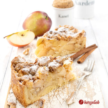 2 Stücke Apfelkuchen oder Streuselkuchen nach einem Apfel-Streuselkuchen Rezept von herzelieb. Im inneren sieht man die üppige Apfelfüllung, auf dem Kuchen die dicken Butterstreusel. Dekoriert Zimtstangen, Äpfeln und Gewürzgefäßen. Neben d den Kuchenstücken liegt eine Kuchengabel.