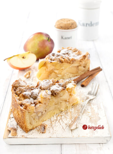 2 Stücke Apfelkuchen oder Streuselkuchen nach einem Apfel-Streuselkuchen Rezept von herzelieb. Im inneren sieht man die üppige Apfelfüllung, auf dem Kuchen die dicken Butterstreusel. Dekoriert Zimtstangen, Äpfeln und Gewürzgefäßen. Neben d den Kuchenstücken liegt eine Kuchengabel.