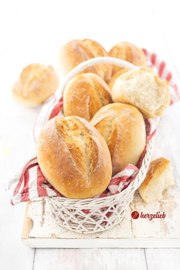 Ein Korb mit Brötchen nach einem Frühstücksbrötchen Rezept im Salz-Hefe-Verfahren, Die Brötchen sind goldbraun gebacken und der Korb ist mit einem rotweiß gestreiftem Tuch ausgeschlagen.