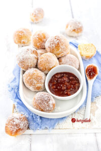 Goldbraun gebackene Quarkbällchen aus der Heißluftfritteuse, die in Zucker gewälzt sind. Mit Erdbeer-Rhabarber-Marmelade angerichtet auf einer weißen Blatte