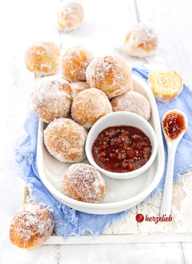 Goldbraun gebackene Quarkbällchen aus der Heißluftfritteuse, die in Zucker gewälzt sind. Mit Erdbeer-Rhabarber-Marmelade angerichtet auf einer weißen Blatte