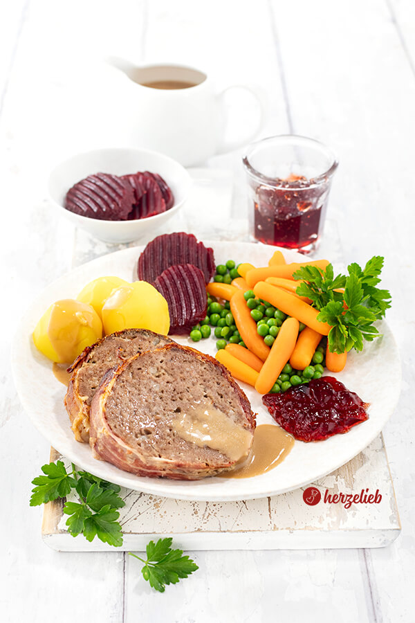 2 Scheiben Hackbraten aus Dänemark nach einem Forloren Hare Rezept von herzelieb. Umwickelt mit knusprigen Bacon. Angerichtet mit Rote Bete, Kartoffeln, Soße roter Johannisbeermarmelade und Erbsen mit Möhren. 