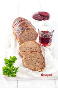 Angeschnittener Hackbraten oder falscher Forloren Hare Rezept von herzelieb aus Dänemark. Umwickelt mit Bacon, vor dem Braten liegen 2 Scheiben davon.Angerichtet auf einem Stück Papier dekoriert mit einem Gläschen rote Johannisbeermarmelade.