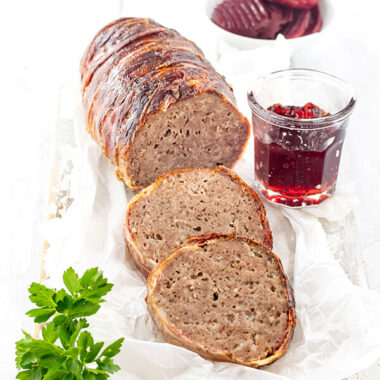 Angeschnittener Hackbraten oder falscher Forloren Hare Rezept von herzelieb aus Dänemark. Umwickelt mit Bacon, vor dem Braten liegen 2 Scheiben davon.Angerichtet auf einem Stück Papier dekoriert mit einem Gläschen rote Johannisbeermarmelade.