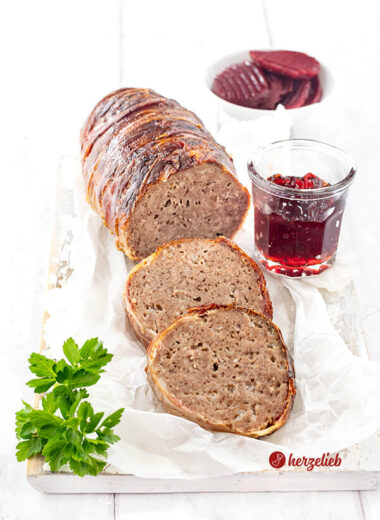 Angeschnittener Hackbraten oder falscher Forloren Hare Rezept von herzelieb aus Dänemark. Umwickelt mit Bacon, vor dem Braten liegen 2 Scheiben davon.Angerichtet auf einem Stück Papier dekoriert mit einem Gläschen rote Johannisbeermarmelade.