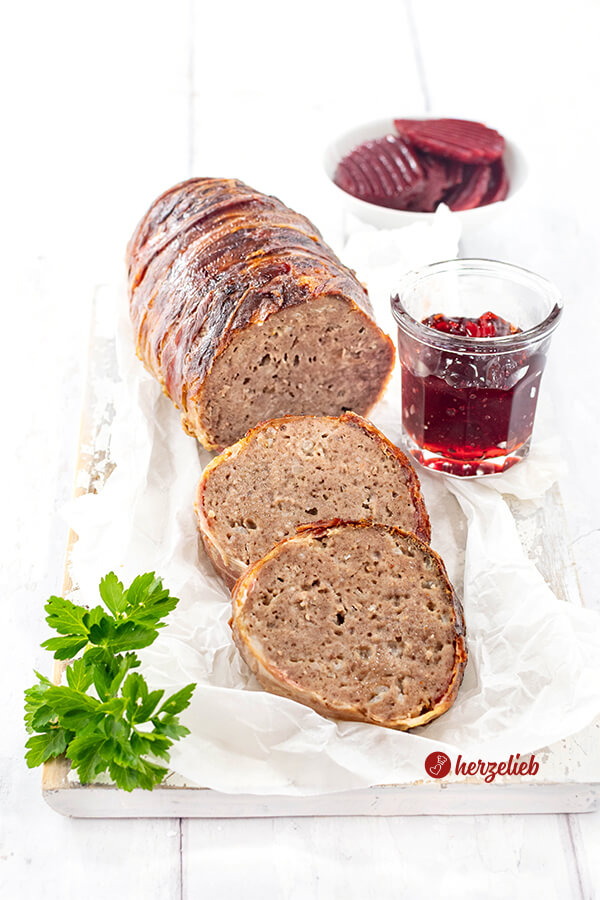 Angeschnittener Hackbraten oder falscher Forloren Hare Rezept von herzelieb aus Dänemark. Umwickelt mit Bacon, vor dem Braten liegen 2 Scheiben davon.Angerichtet auf einem Stück Papier dekoriert mit einem Gläschen rote Johannisbeermarmelade.