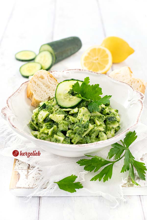 Kohlsalat oder Gurkensalat mit einem grünen Dressing nach einen Grüne Göttin Salat Rezept von herzelieb. Dekoriert mit Gurkenscheiben und glatter Petersilie. Im Hintergrund eine halbe und eine ganze 