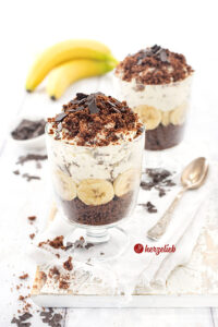 Ein Nachtisch nach einem Maulwurfkuchen Dessert im Glas mit Schokokuchen, Bananenscheiben, Sahnecreme und Schokoraspeln, dekorativ geschichtet und mit Schokoraspeln bestreut.