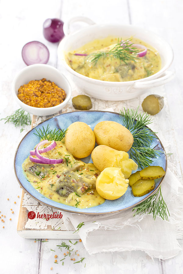 Ein Teller mit Sennepssild aus Dänemark nach eiem Senfhering Rezept von herzelieb. Angerichtet mit Pellkartoffeln, Dill, Gurke, roten Zwiebeln Im Hintergrund eine Schale Senf und eine Schale mit dem eingelegtem Hering.