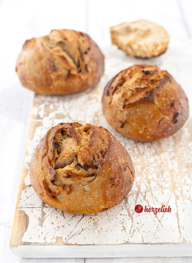 Drei frisch gebackene Röstzwiebelbrötchen mit knuspriger, goldbrauner Kruste liegen auf einem weißen, leicht abgenutzten Holzbrett.