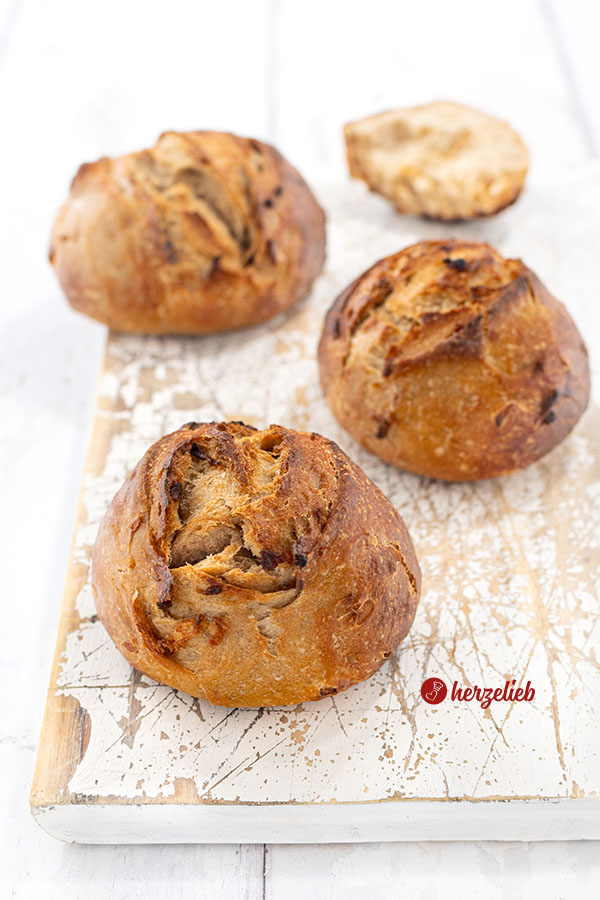 Drei frisch gebackene Röstzwiebelbrötchen mit knuspriger, goldbrauner Kruste liegen auf einem weißen, leicht abgenutzten Holzbrett.