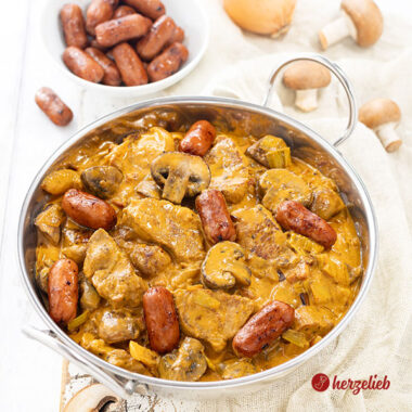 Eine Edelstahl-Servierschale mit einem Wikingertopf aus Dänemark nach einem Vikingegryde Rezept von herzelieb. Im Hintergrund eine Schale mit Cocktailwürstchen, Zwiebeln und braune Champignons.