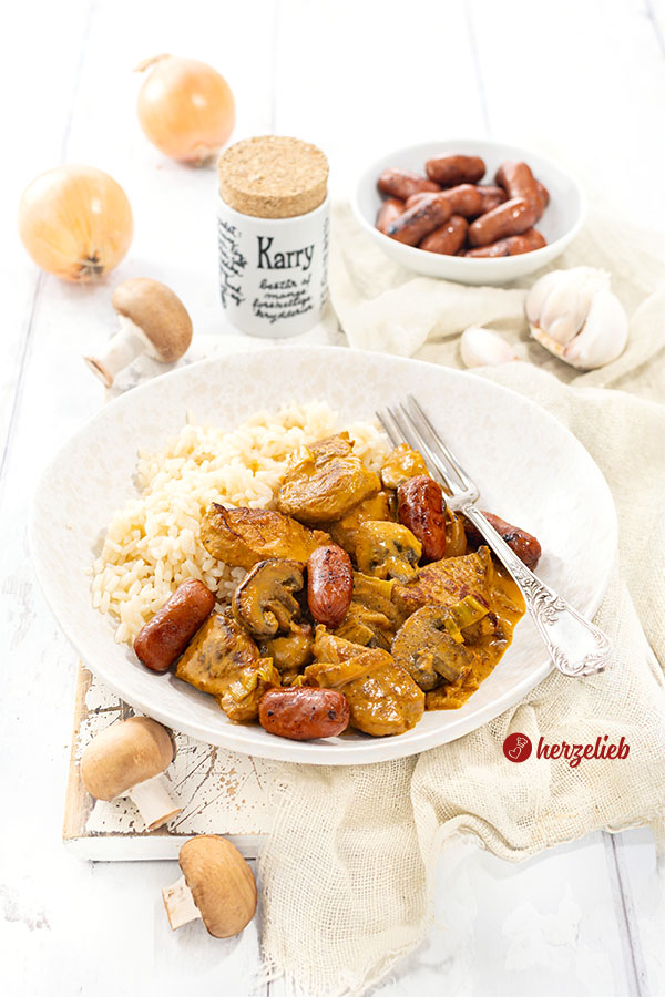 Ein Teller mit einem Filettopf nach einem Vikingegryde Rezept aus Dänemark von herzelieb. Der Wikingertopf ist angerichtet mit Reis m Vordergrund und Hintergrund Pilze. Hinten Zwiebeln, ein Gewürzgefäß und eine Schale mit Pilzen