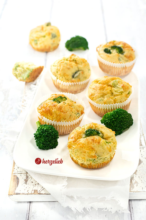 6 herzhafte Muffins nach einem Brokkoli-Käse-Muffins Rezept von herzelieb auf einem weißen Teller. Dekoriert mit Brokkoliröschen.