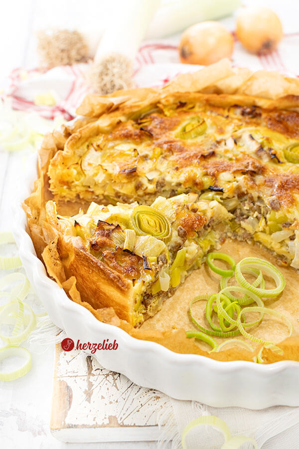 Eine Tarteform mit einer Käse-Lauch-Tarte mit Hackfleisch. Goldbraun gebacken und mit Lauchringen dekoriert.