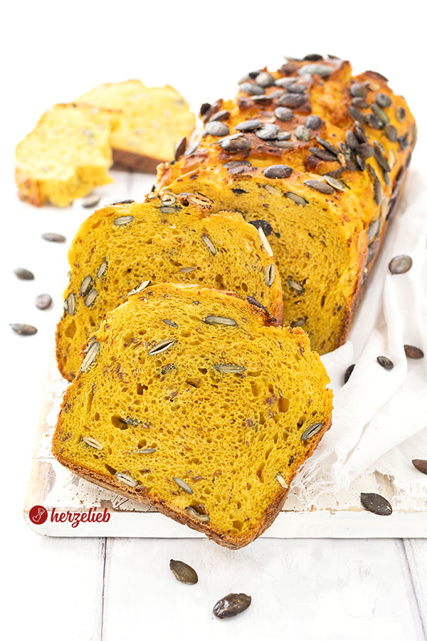 Ein saftiges und angeschnittenes Kürbisbrot oder Buttermilchbrot nach einem Kürbis-Buttermilchbrot Rezept von herzelieb. Zwei Scheiben davon lieben vor dem angeschnittenen Brotlaib.