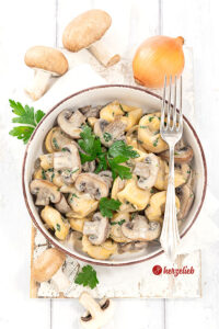 Eine Schale mit einem Pastagericht nach einem Pilz-Tortellini-Topf Rezept von herzelieb. In der Schüssel Tortellini, Pilze und eine helle Soße. Dekoriert mit Petersilie