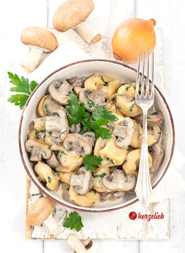 Eine Schale mit einem Pastagericht nach einem Pilz-Tortellini-Topf Rezept von herzelieb. In der Schüssel Tortellini, Pilze und eine helle Soße. Dekoriert mit Petersilie