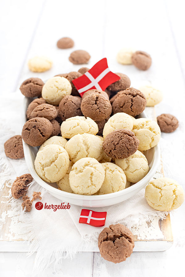 Eine Platte mit hellen und dunklen Plätzchen aus Dänemark nach einem Fedtkager Rezept von herzelieb. Zwischen den Plätzchen und vor der Platte liegt je ein Dannebrog. Rings um die Porzellanplatte liegen weiter Kekse.